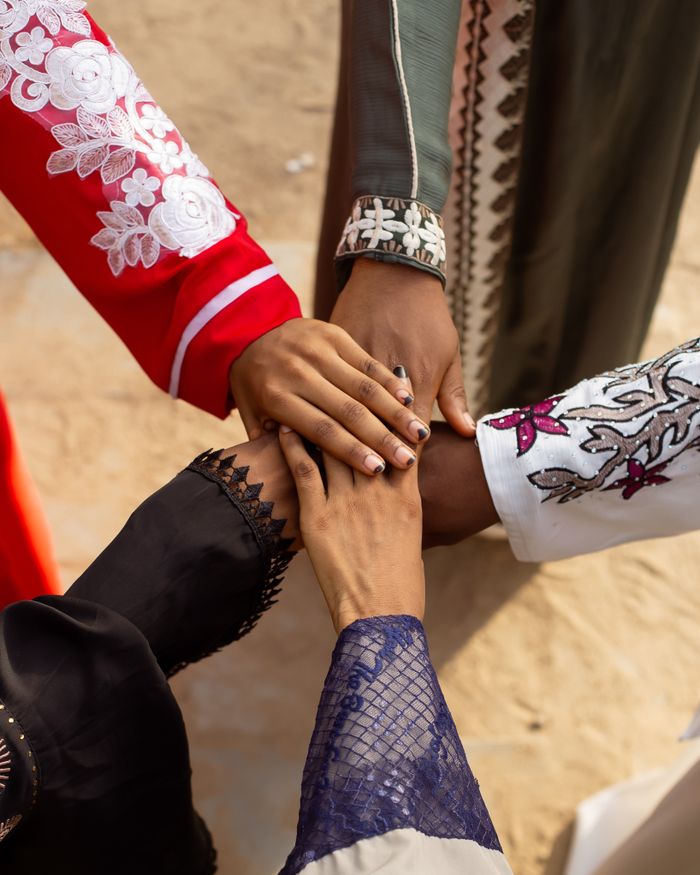 A group of people joining hands wearing colorful traditional attire outdoors, symbolizing unity.