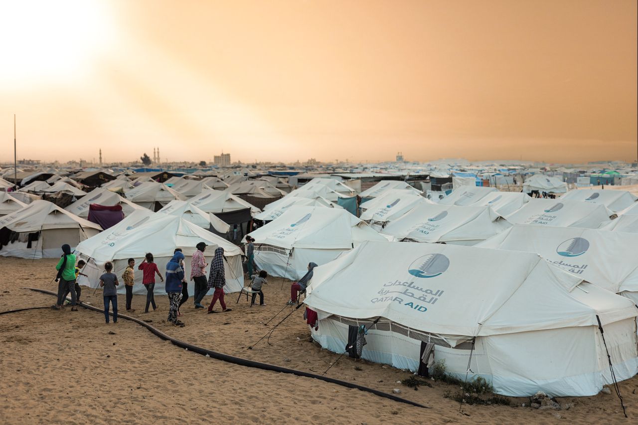 A crowded refugee camp with aid tents at sunset, highlighting human resilience.